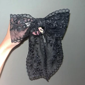 Svart spets rosett - Superfint stor rosett i spets och broderade blommor. Rosetten har vågiga kanter och fästs enkelt med ett metallspänne. Aldrig använd 