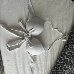 Vit bikini med knyt och vadderade kupor - Snygg vit bikini med vadderade kupor och knyt framtill. Bikinin har en enkel och stilren design med smala axelband och mjukt material som känns skönt mot huden. Perfekt för lata dagar på stranden eller vid poolen.