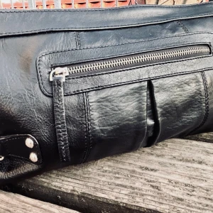 Clutch i skinn från Wera! - Stor svart clutch i skinn med flera fack, dragkedja och snygga detaljer från Wera. Mått: 35 x 20 cm. Jättebra skick!