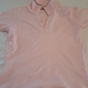 Ljusrosa pikétröja från Joy - Snygg ljusrosa pikétröja från Joy med klassisk krage och kort ärm. Tröjan har en beige kant på kragen och är tillverkad i mjuk bomull. Perfekt för en chill och stilren look. Tröjan är storlek M men passar även mig som har storlek xs-s och är 168 lång. Jag är också villig att diskutera priset