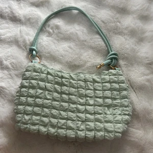 Mintgrön quiltad axelväska - Superfin mintgrön axelväska med quiltad struktur och mjukt tyg. Väskan har ett handtag med snygga knutdetaljer och guldfärgade ringar. Stängs med dragkedja och har ett rymligt innerfack. Perfekt för att lyfta din outfit med en cool pastellfärg.