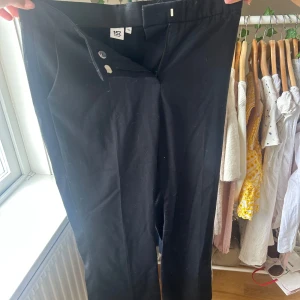 Svarta kostymbyxor från 157 - Klassiska svarta kostymbyxor från 157 med rak passform och diskret knapp- och dragkedjestängning. Snygga till skjorta eller t-shirt, perfekta för en clean och stilren look. Gjorda i ett mjukt bomullsmaterial som känns bekvämt hela dagen.