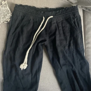 Svarta linnebyxor med snörning - Svarta linnebyxor från Roxy med bred resår i midjan och vit snörning framtill. Byxorna har raka ben, stora fickor både fram och bak samt en avslappnad passform. Perfekta för chill dagar eller när du vill ha en skön och luftig stil.