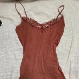 Rödbrun linnetopp med spets - Supersnygg  linnetopp med tunna axelband och v-ringning dekorerad med blommig spets. Mjuk och skön.