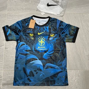 Nike Brasil fotbollströja  - Snygg Brasilien fotbollströja från Nike med ett stort blått pantermotiv och gula detaljer. Tröjan är kortärmad, har svart krage och är tillverkad i Dri-FIT material som andas. Perfekt för dig som vill sticka ut på planen eller läktaren.