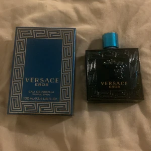 Versace Eros Eau de Parfum 100ml/55ml - Versace Eros Eau de Parfum ungefär 55ml kvar med ikonisk blå glasflaska och guldtext. Flaskan har ett Medusa-huvud i relief och geometriskt mönster. Kommer med matchande blå kartong med silverdetaljer. Lyxig och stilren doft för dig som gillar statement-parfymer.