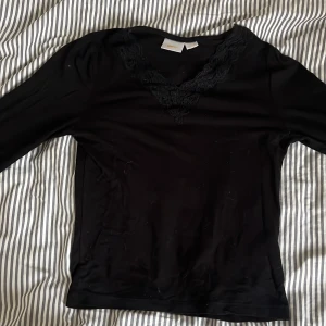 Svart spetsdetaljerad topp Gina Tricot - Svart långärmad topp från Gina Tricot med snygg v-ringning och spetsdetaljer runt halsen. Tunn och mjuk känsla, perfekt att styla med jeans eller kjol. Enkel men ändå med en extra touch tack vare spetsen.