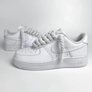 Nike Air Force 1 Rope Laces - Klassiska Nike Air Force 1 sneakers i helvitt skinn med chunky, rep-liknande snörning. Snygg och clean design med perforerad tå och låg profil. Perfekta för dig som vill sticka ut med en unik twist på en ikonisk modell.