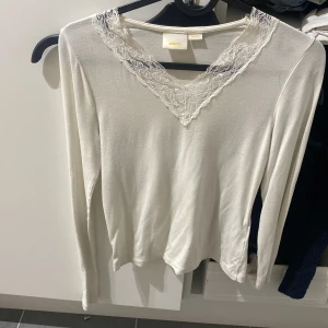 Vit långärmad topp med spets från Glamtool - Supersöt vit långärmad topp från Glamtool med v-ringning och fina spetsdetaljer runt halsen. Tunn och mjuk, perfekt att styla med jeans eller kjol. Enkel men ändå elegant vibe.