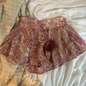 Mönstrade shorts med tofsar från H&M - Superfina shorts från H&M i beige och lila med paisleyinspirerat mönster. Lätt och flowigt material i polyester, midwaist med smock i midjan och snörning med dekorativa tofsar och pärlor framtill. Perfekta för sommarens varma dagar.