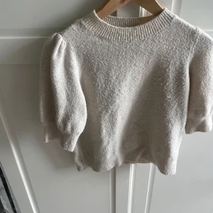 Beige stickad tröja Vero Moda XS - Supersöt beige stickad tröja från Vero Moda i storlek XS. Tröjan har puffiga korta ärmar och ribbad halsringning. Perfekt för dig som gillar en mjuk och mysig look med lite volym på axlarna. Enkel att matcha med både jeans och kjol.