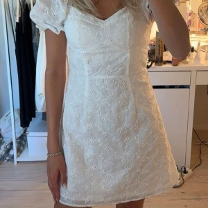 Vit kort klänning med puffärm - Superfin vit kort klänning med broderade blommor och puffiga korta ärmar. Söt v-ringning och figurnära passform. Endast använd en gång 