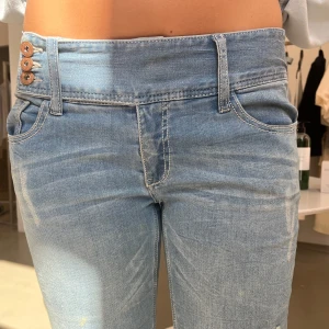 Ljusblå bootcut jeans med slitningar - Säljer ett par ljusblå jeans med bootcut-modell och slitna detaljer framtill samt fransade benslut. Är väldigt korta på mig eftersom jag är 180!! Byxorna har låg midja, klassiska fem fickor och stängs med tre knappar. 