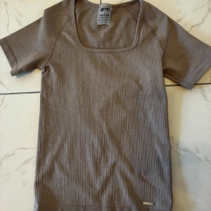 Ribbad brun topp från Aim'n - Säljer en ribbad brun topp från Aim'n med fyrkantig ringning och korta ärmar. Toppen är i ett stretchigt material av polyester och elastan. Liten i storleken, passar xs.