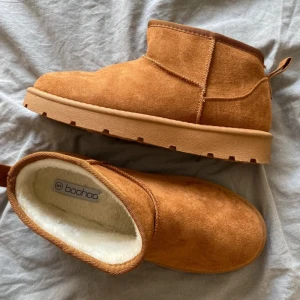 Bruna mockaboots från Boohoo - Mysiga boots i brun mocka från Boohoo med rund tå och platt sula. Insidan är fodrad med mjukt vitt foder. Använda en gång.