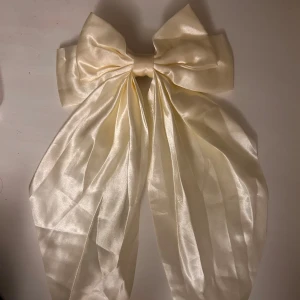 Stor cremefärgad satinrosett diadem - En riktigt stor och lyxig cremefärgad rosett i glansig satin med hårspänne på baksidan, passar snyggt i håret och ger en elegant vibe. 💕 Rosetten är bred och har långa band som hänger ner.