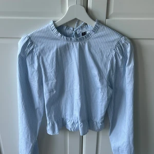 Blåvit randig blus med volang  - Supersöt blus från H&M i blåvitt randigt med långa ärmar, volangkant nertill och vid halsen. Blusen har knytning i nacken och lätt puffade axlar 🩵Använd max 3 ggr. Fler bilder kan fixas!