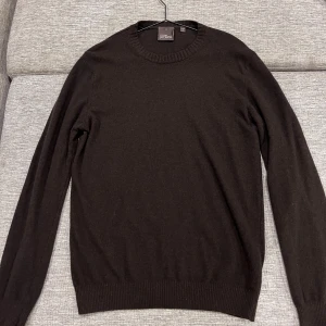 Mörkbrun kashmirtröja Oscar Jacobson - Säljer en stilren mörkbrun rundhalsad tröja från Oscar Jacobson i mjuk kashmir. Tröjan har ribbade muddar vid ärmslut och nederkant samt lång ärm. Perfekt att bära över skjorta för en clean look.