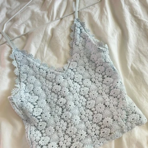 Ljusblå virkad croppad linnetopp - Superfin ljusblå croppad linnetopp med virkade blommor och smala axelband. Toppen har v-ringning och är perfekt för varma dagar. 