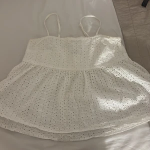 Vit broderad linnetopp med spets - Superfin vit linnetopp med tunna axelband och broderade hålmönster över hela tyget. Toppen har en volang nertill och är perfekt för varma dagar. Söt spetskänsla och luftig passform , storlek L från bikbok!