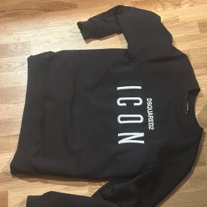 DSQUARED2 - Svart sweatshirt från DSQUARED2 i storlek M med stor vit broderad text 'ICON' och DSQUARED2-logga på bröstet. Klassisk rund halsringning och ribbade muddar. Tillverkad i mjuk bomull för en skön och avslappnad stil.