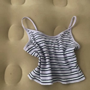 Randig ribbad linnetopp från FB SISTER - Superfin ribbad linnetopp från FB SISTER i storlek L. Toppen är vit med svarta och lila ränder, har smala axelband och croppad passform. Perfekt för varma dagar och enkel att styla med jeans eller kjol.