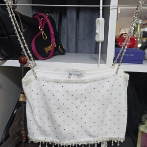 Vit glittrig tubtopp från ZARA - Supersöt vit tubtopp från ZARA med glittriga stenar och pärldetaljer längst ner. Toppen har ribbad struktur och tunna axelband med strass som ger extra bling. Perfekt för dig som vill sticka ut och glänsa lite extra!
