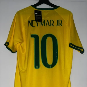 Brasilien Neymar Jr 10 Nike fotbollströja - Gul Brasilien fotbollströja från Nike med gröna detaljer, Neymar Jr och nummer 10 på ryggen. Klassisk CBF-logga på bröstet och korta ärmar. Tillverkad i lätt och ventilerande material, perfekt för match eller träning.
