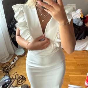 Vit kortklänning med volangärmar - Supersnygg vit kortklänning med djup v-ringning och stora volangärmar. Klänningen har en figurnära passform och markerad midja, perfekt för dig som vill sticka ut. Materialet känns mjukt och följsamt mot kroppen.