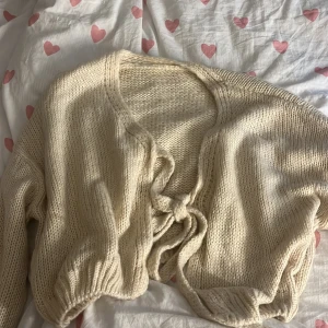 Beige stickad kofta med knyt - Supermysig beige stickad kofta med knyt framtill. Koftan har långärmade ärmar och ribbade muddar vid ärmslut och nederkant. Perfekt att slänga över en topp för en chill och snygg look.