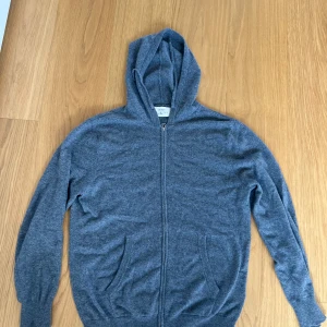 Grå kashmirhoodie från Zara Origins - Mjuk och lyxig grå hoodie i 100% kashmir från Zara Origins. Tröjan har dragkedja framtill, huva och två fickor. Perfekt för dig som vill ha en stilren och bekväm look med premiumkänsla. Långärmad och med ribbade muddar för extra komfort.