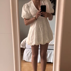 Vit kortklänning med puffärm - Supersöt vit kortklänning med puffiga ärmar och v-ringning. Klänningen har ett broderat blommönster och ballongformad kjol som ger en trendig och lekfull look. Perfekt för sommarens alla tillfällen och ger en fräsch vibe. Men även perfekt som student klänning