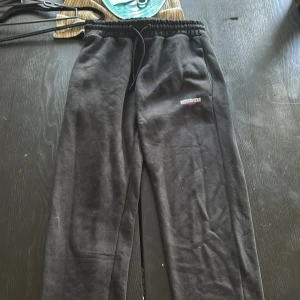 Svarta mjukisbyxor från McKenzie S - Svarta mjukisbyxor från McKenzie med dragsko i midjan och broderad logga på låret. Byxorna har en relaxed fit och är gjorda i mjukt material som passar perfekt för chill dagar eller träning.