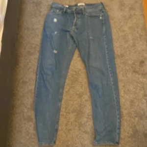 Blå jeans Jack & Jones 31/34 - Säljer ett par klassiska blå jeans från Jack & Jones i storlek 31/34. Jeansen har normal passform, raka ben och är tillverkade i slitstarkt denim. Snygga slitningar framtill för en trendig look. Egna gjorda slitningar inte från originalet! Knappt använda! Ny pris 650kr frågor o funderingar tveka inte på att höra av er!