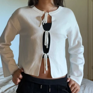 Vit kofta med snörning från Gina Tricot - Superfin vit kofta från Gina Tricot med tre snörningar framtill som ger en trendig look. Långärmad och croppad modell med rund halsringning. Perfekt att styla med höga jeans eller kjol för en cool vibe. Helt ny och använd bara 1 gång.