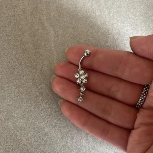 Navelpiercing med Blomsterhänge silver  - Säljer en oanvänd Navelpiercing med  Blomsterhänge silver   Längd : 10mm Material  Stav : Kirurgisk Stål (Finns i guld oxå oanvänd!)