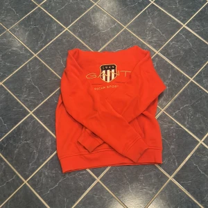 Röd sweatshirt från Gant - Riktigt snygg röd sweatshirt från Gant med broderad logga och text framtill. Klassisk passform med rund hals och långa ärmar. Perfekt för dig som gillar sportig och stilren vibe. Men också perfekt för dig som vill sticka ut lite till sommaren till exempelvis ” linne byxor ” 
