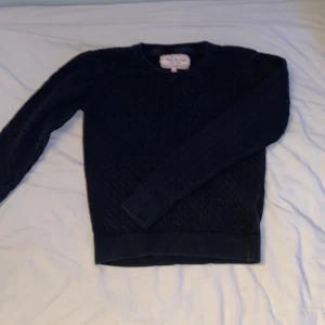 svart stickad tröja från C'est la vie - Mysig svart stickad tröja från C'est la vie med diskret strukturmönster. Tröjan har rund halsringning och långa ärmar, perfekt för lager-på-lager under kyliga dagar. Enkel och stilren design som funkar till det mesta.