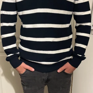 Marinblå half zip-tröja - Snygg stickad tröja från H&M i marinblått med vita ränder. Tröjan har en half zip-dragkedja vid halsen och är långärmad.