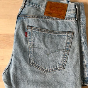 Levi's 501 ljusblå jeans W31 L32 - Klassiska Levi's 501 jeans i ljusblå denim med raka ben och normal passform. Ikonisk läderpatch bak i midjan och röd Levi's-tagg på bakfickan. Perfekta för en avslappnad och tidlös stil.