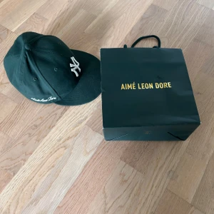 Aimé Leon Dore new era  - Snygg mörkgrön keps från Aimé Leon Dore i samarbete med New York Yankees. Klassisk basebollmodell med böjd skärm, broderad NY-logga framtill och Aimé Leon Dore-text på sidan. Tillverkad i bomull och perfekt för en streetwear-look.