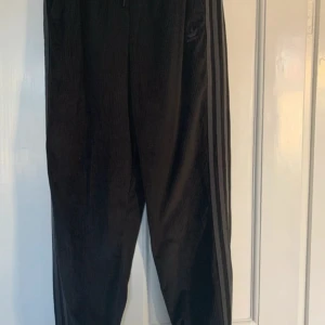 Svarta Adidas Originals byxor  - Svarta byxor med gråa ränder på sidorna som har en en avslappnad vibe. Tyget är som manchesteraktigt och byxorna är jättesköna och i nyskick.