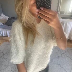Vit fluffig stickad tröja - Supermjuk och fluffig vit stickad tröja med korta ärmar och rund hals. Tröjan har en lätt glittrig känsla i materialet och är perfekt för dig som gillar en cozy och trendig vibe. Passar snyggt till både jeans och kjol.
