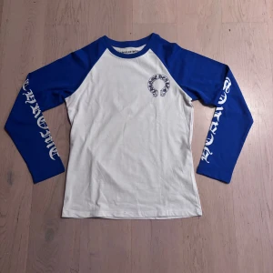 Chrome Hearts långärmad  - Snygg långärmad tröja från Chrome Hearts med blå ärmar och vit kropp. Tryck med logga på bröstet, och deras CH bokstäver på ryggen. Tröjan är i storlek M, fick tröjan av min kusin men jag säljer den för den inte riktigt är min stil 