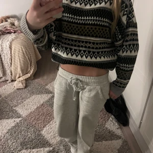 Mönstrad stickad tröja i jordnära toner - Säljer en stickad tröja med snyggt mönster i svart, vitt, grått och brunt. Tröjan har rund hals, långa ärmar och ribbade muddar. Perfekt för dig som gillar en chill och trendig vibe med lite retrofeeling.