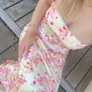 Blommig  långklänning - Superfin axelbandslös långklänning i ljusgul satin med blommigt mönster i rosa, grönt och orange. Klänningen har öppen rygg med snörning  💛🌸
