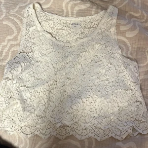 Vit spetsig linnetopp från Monki - Superfin vit linnetopp från Monki i spets med blommigt mönster. Toppen är ärmlös och har en croppad passform med vågig kant nedtill. Perfekt för sommarens alla tillfällen när du vill känna dig extra söt.