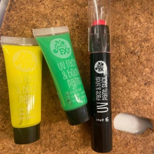 Neon färg - Tre färgglada UV face & body paints från Joker FX: en gul och en grön i tub samt en röd paint stick i svart hylsa. Perfekt för kreativa sminkningar och festivaler. Lätta att applicera och syns i UV-ljus. Neonfärg 