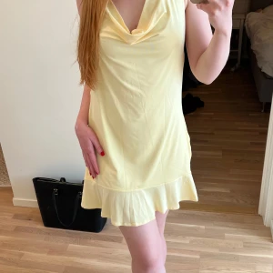 Ljusgul kort klänning Pull&Bear - Säljer ny med lapparna kvar pga råkade beställa för stor storlek och han inte returnera i tid. Supersöt ljusgul kort klänning från Pull&Bear med volangkant nertill, draperad urringning och öppen rygg med knyt. Perfekt för sommardagar och har en riktigt fräsch vibe. Tillverkad i mjuk polyester som känns skön mot huden. 
