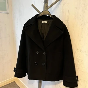 Svart kappa från Desing By Si - Stilren svart kappa med breda slag och dubbelknäppning framtill. Jackan har långa ärmar med knappar vid ärmslut. Använd fåtal gånger☺️ skriv för privata bilder 